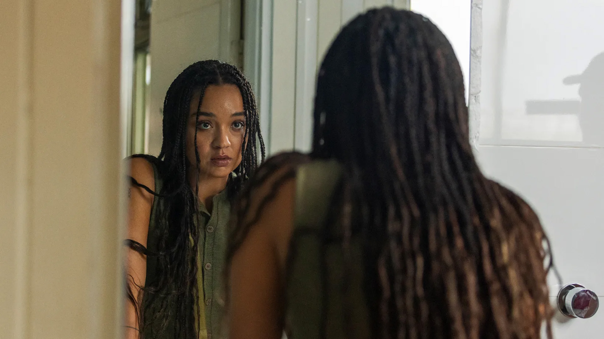 Aisha Dee as Lina in Watching You, looking into a mirror.