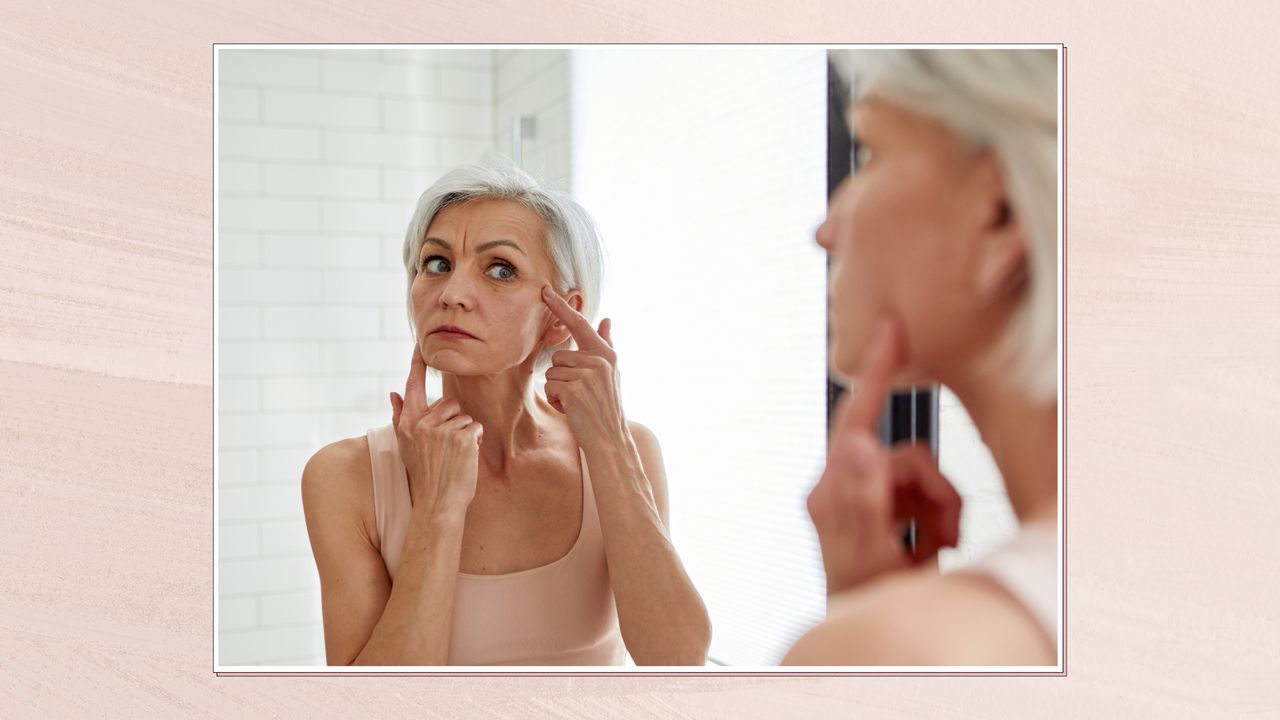 Image of a woman examining her skin in the bathroom mirror, in a white frame against a dusky pink watercolour-style background