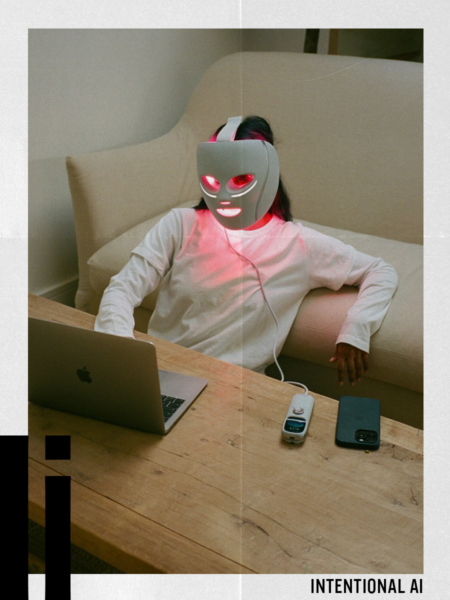 A woman wearing an LED mask typing at a laptop