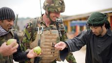 A British soldier (C) and his interpreter (L) talk with an Afghan actor playing the part of a villager during a training exercise in a new "Afghan village" at a military base in Norfolk, in e