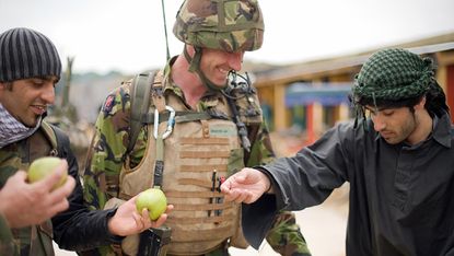A British soldier (C) and his interpreter (L) talk with an Afghan actor playing the part of a villager during a training exercise in a new "Afghan village" at a military base in Norfolk, in e