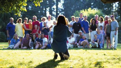 A woman takes a family photo of a large family group on a sunny day.