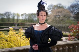 Suranne Jones as Anne Lister in Gentleman Jack standing on a terrace in a dark blue dress with a feather in her hair.