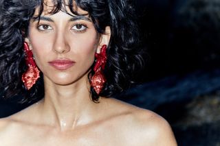 A model wears large Julietta red seashell earrings with a conch shell and red starfish