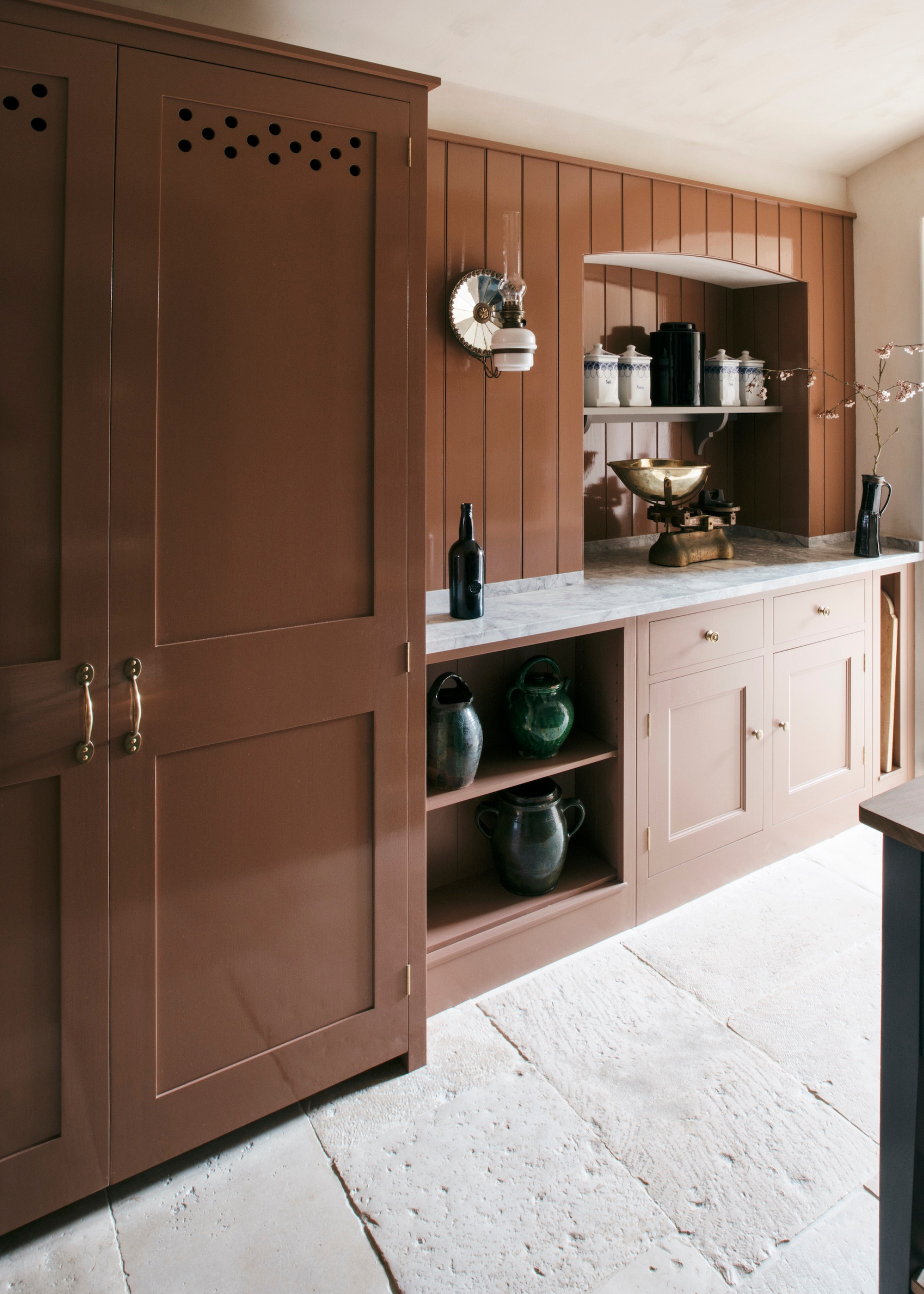 A brown terracotta kitchen in a traditional stye with a stone floor, marble worktop and open shelving.