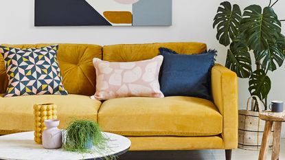 Mustard sofa with coloured cushions by artwork and houseplant