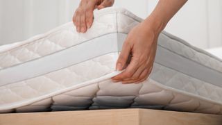 A person lifts up the edge of a mattress before flipping it