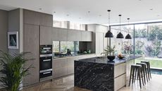 A neutral kitchen with black marble island, black stools, and wooden cabinets.