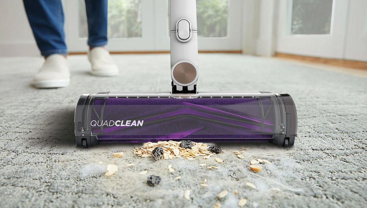 Closeup of purple cordless vacuum cleaner head vacuuming oats and dust from gray carpet.