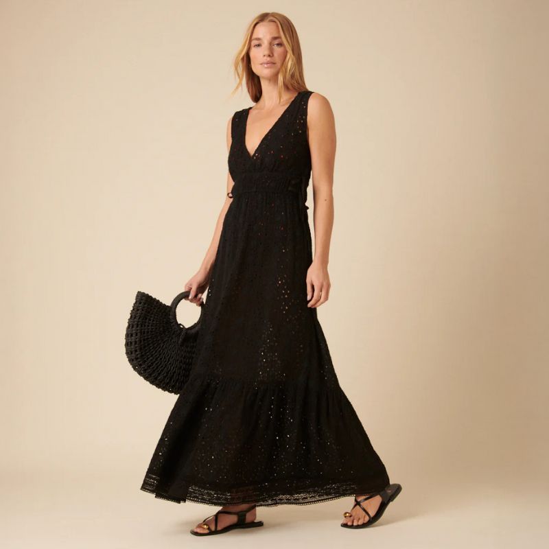 A woman carries a straw bag while wearing a black broderie Nobody's Child midi dress