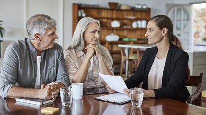 A financial adviser talks with an older couple at their dining room table.