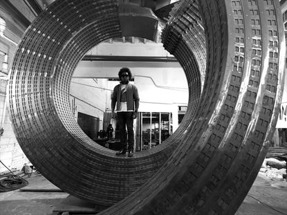 Black and white image of Alexandre Arrechea stood on his -in-progress reinterpretation of the Sherry Netherland Building, in a workshop setting
