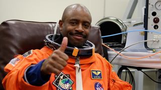 astronaut leland melvin in an orange flight suit giving a thumbs up