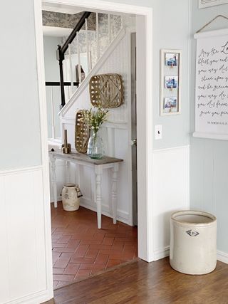 freehand stencilling on an entryway wall with a herringbone pattern, with tiled floor in the entry and wooden floor in the foreground, a console table, and pictures and art on the walls