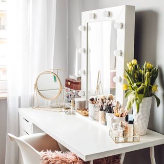 Light and bright beauty vanity table set-up with cosmetics mirror, fresh florals, white vanity table, and styled arrangement of makeup pots