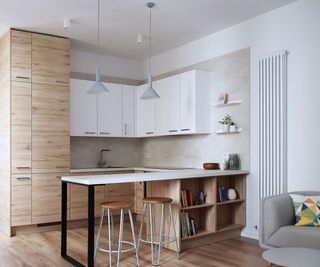 A small kitchen area in the corner of an open plan living room. There is a column radiator on the wall