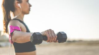 Woman outdoors holding a dumbbell in right hand with arm lifted to the side