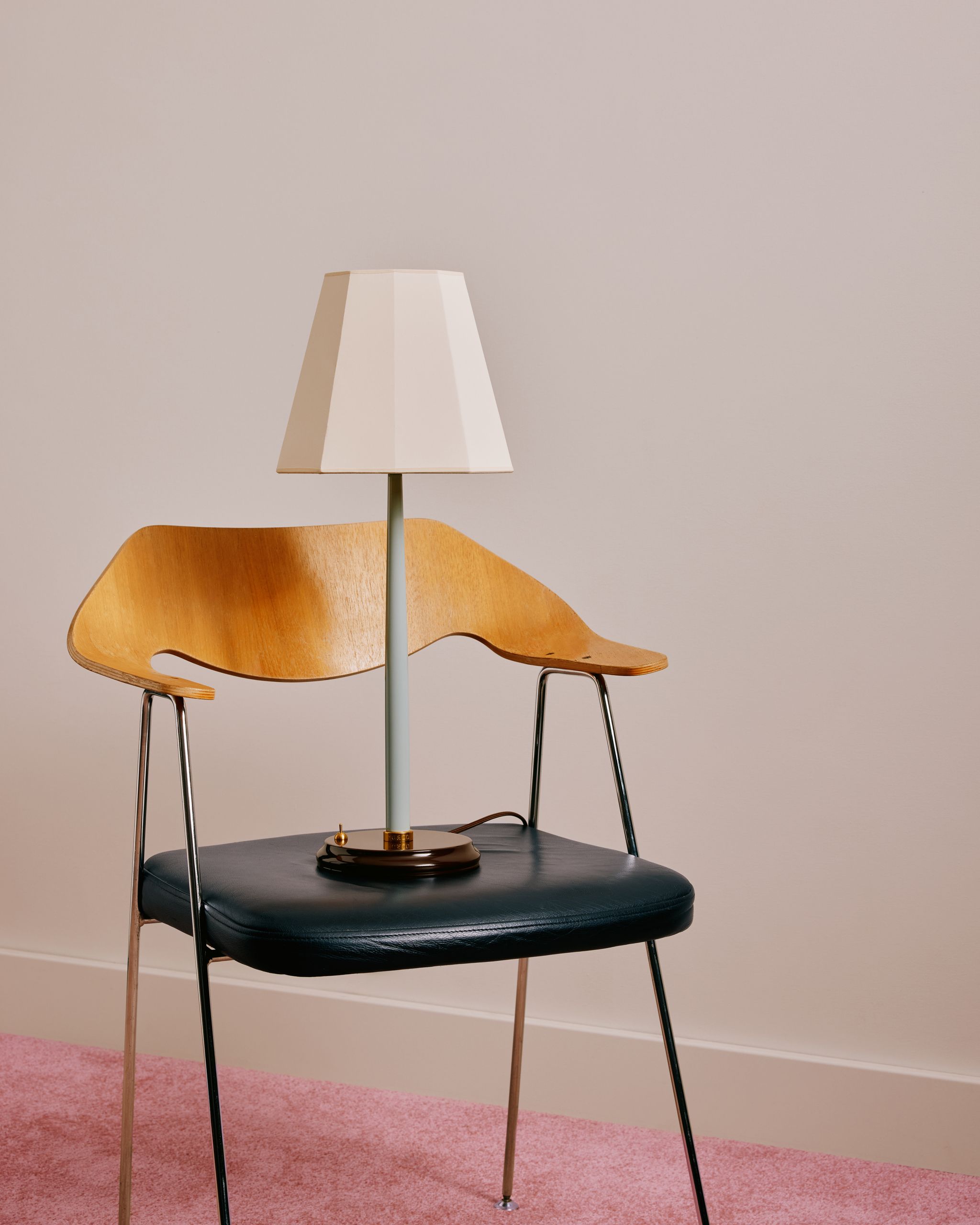 A light blue table lamp on a wooden and black leather chair in a white room with pink rugs.