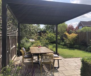 A small UK garden with a pergola covering an outdoor seating area on a natural stone patio