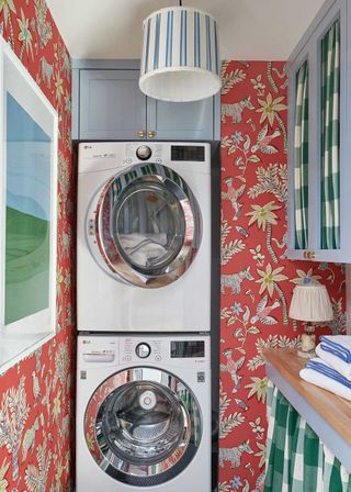 small laundry room with red patterned wallpaper and stacked appliances