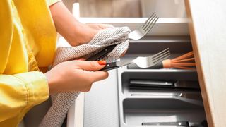 Woman holding two forks above an open cutlery drawer
