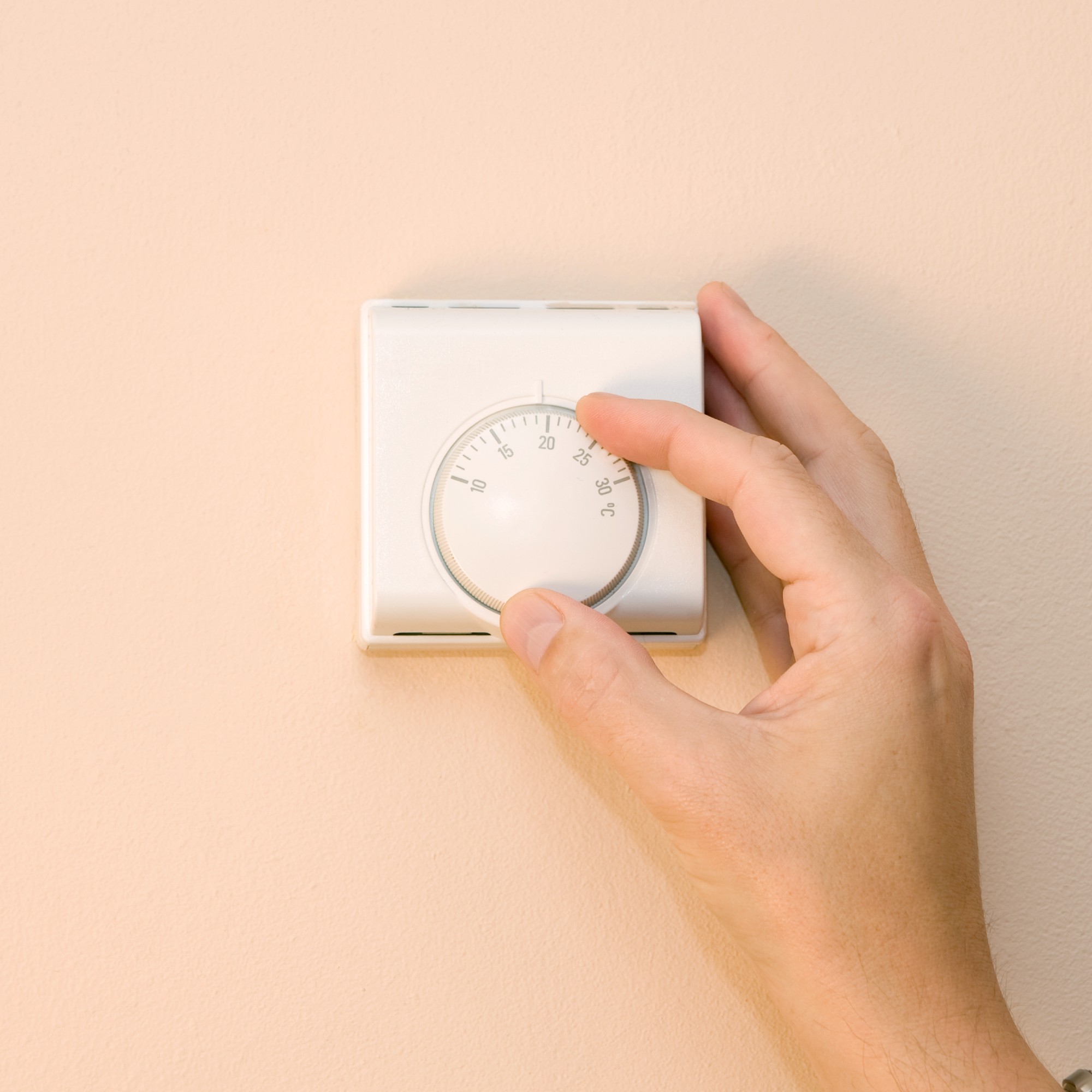 Hand turning thermostat on peach wall