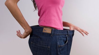 A woman tries on a pair of jeans that is much too big.