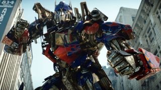 Still from a Transformers movie. Here we see the Transformer Optimus Prime (large blue and red robot that can turn into a truck). He is standing in a city full of skyscrapers, in a fighting ready pose.