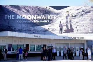 a large mural of an astronaut on the moon is seen above the ticket counter at the entrance to a museum