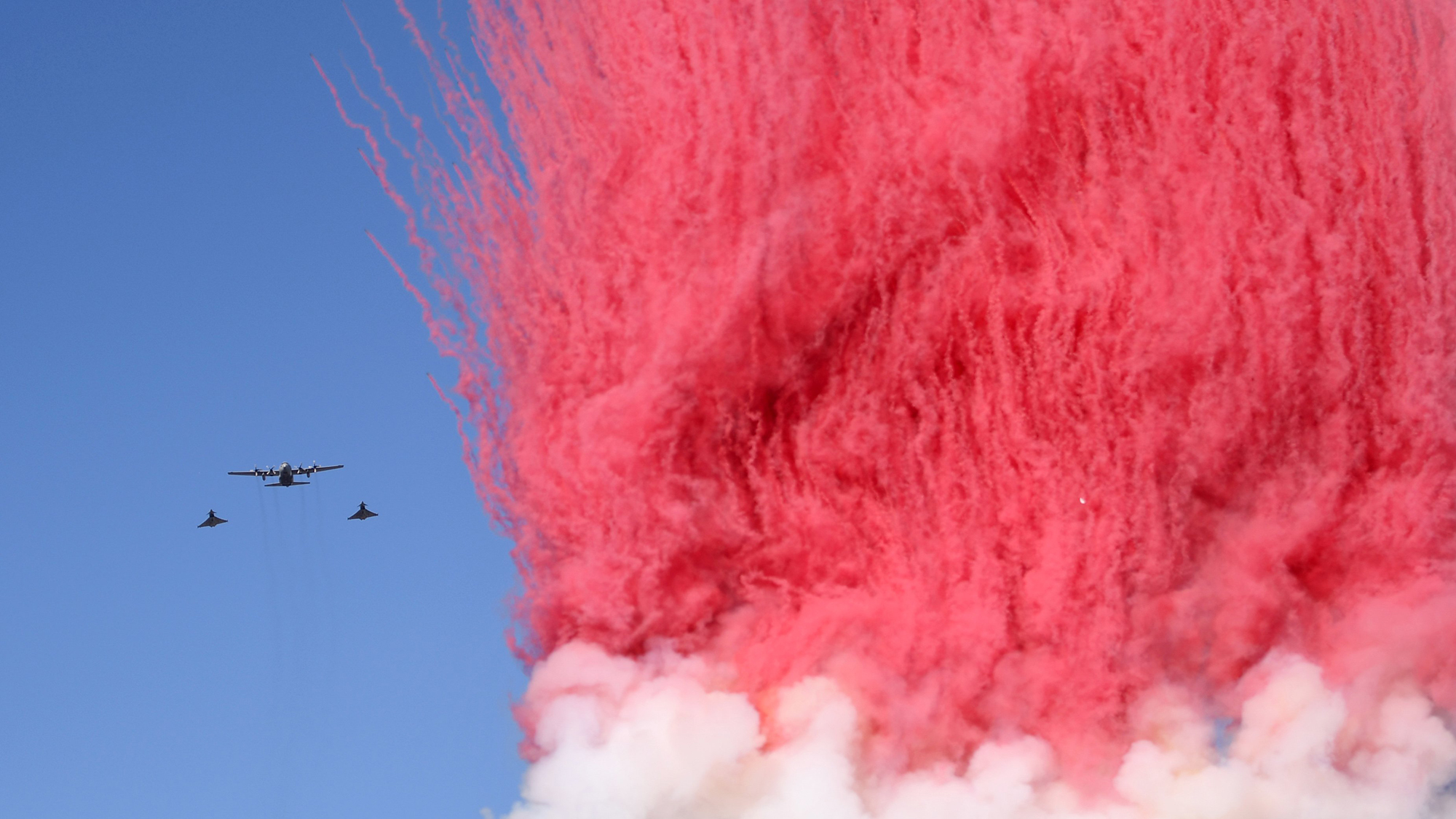 Aircraft fly alongside a wall of brightly colored smoke during the National Day celebrations in Vienna, Austria