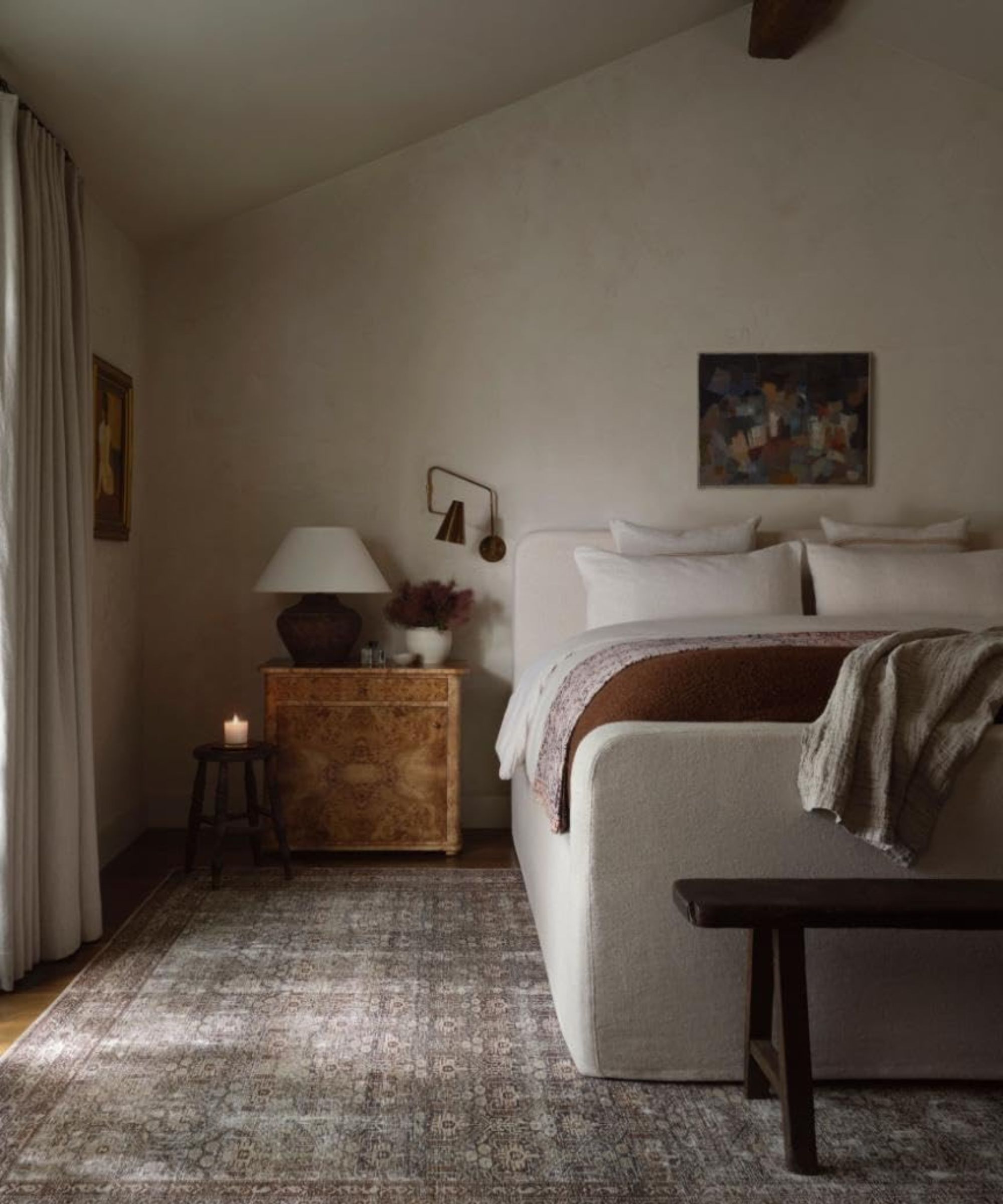 moody vintage style bedroom with a linen slipcovered bed, grey printed rug, burl wood nightstand and vintage decor
