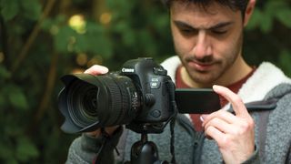 man using Canon EOS 6D Mark II to shoot video, looking at the fold-out LCD screen