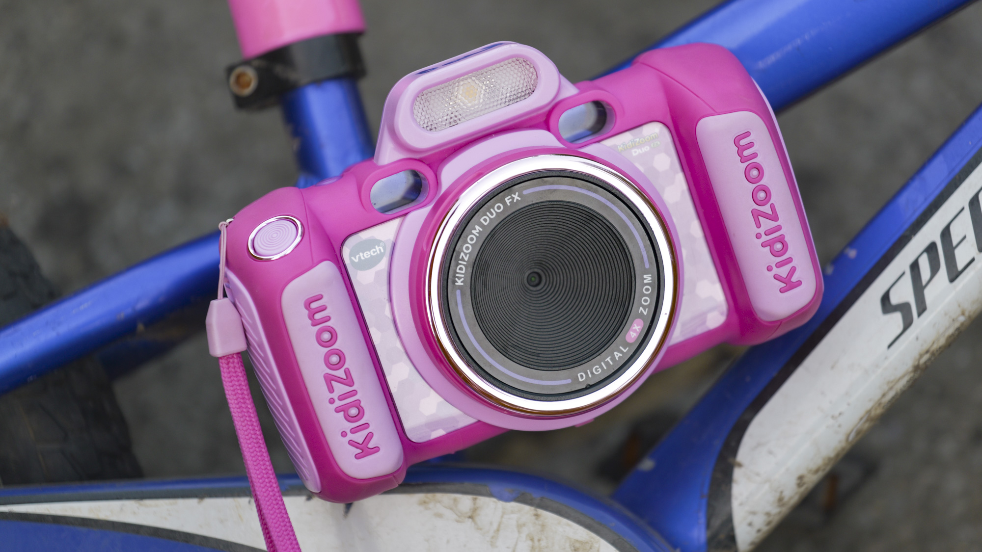 A pink V-Tech KidiZoom Duo camera resting on the blue and white frame of a kid's bike
