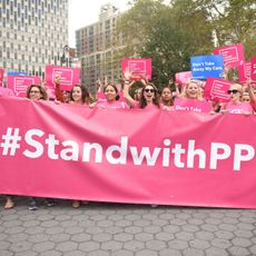 Protestors dressed in pink t-shirts holding aa banner that reads "#StandwithPP"