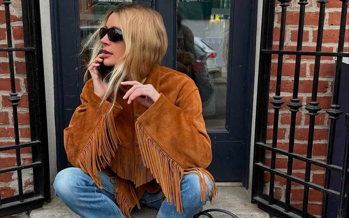 Courtney Grow wears a brown suede fringed jacket with jeans and flats on a New York city stoop.