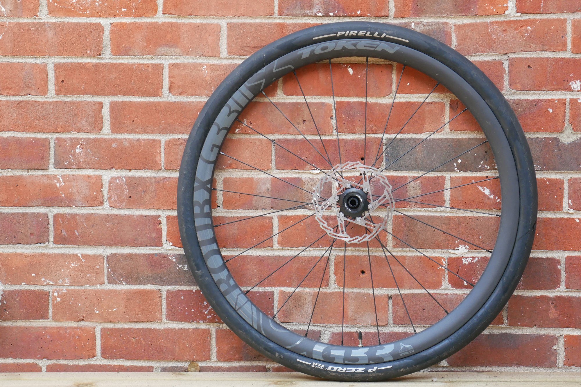 A black Pirelli P-Zero Race TLR tyre with white writing mounted to a Token wheel in front of a red brick wall