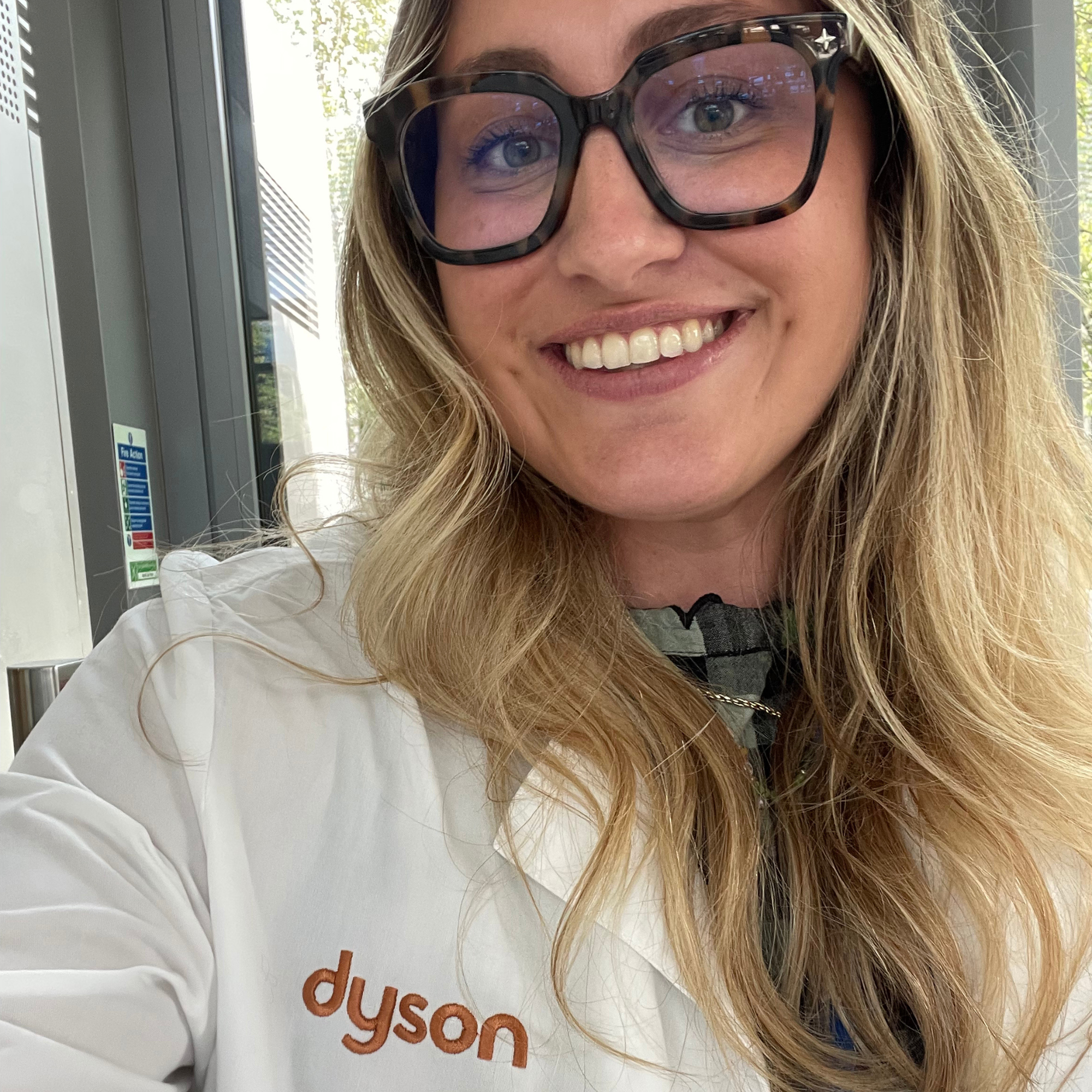 Woman in glasses with long blonde hair wearing white Dyson-branded lab coat