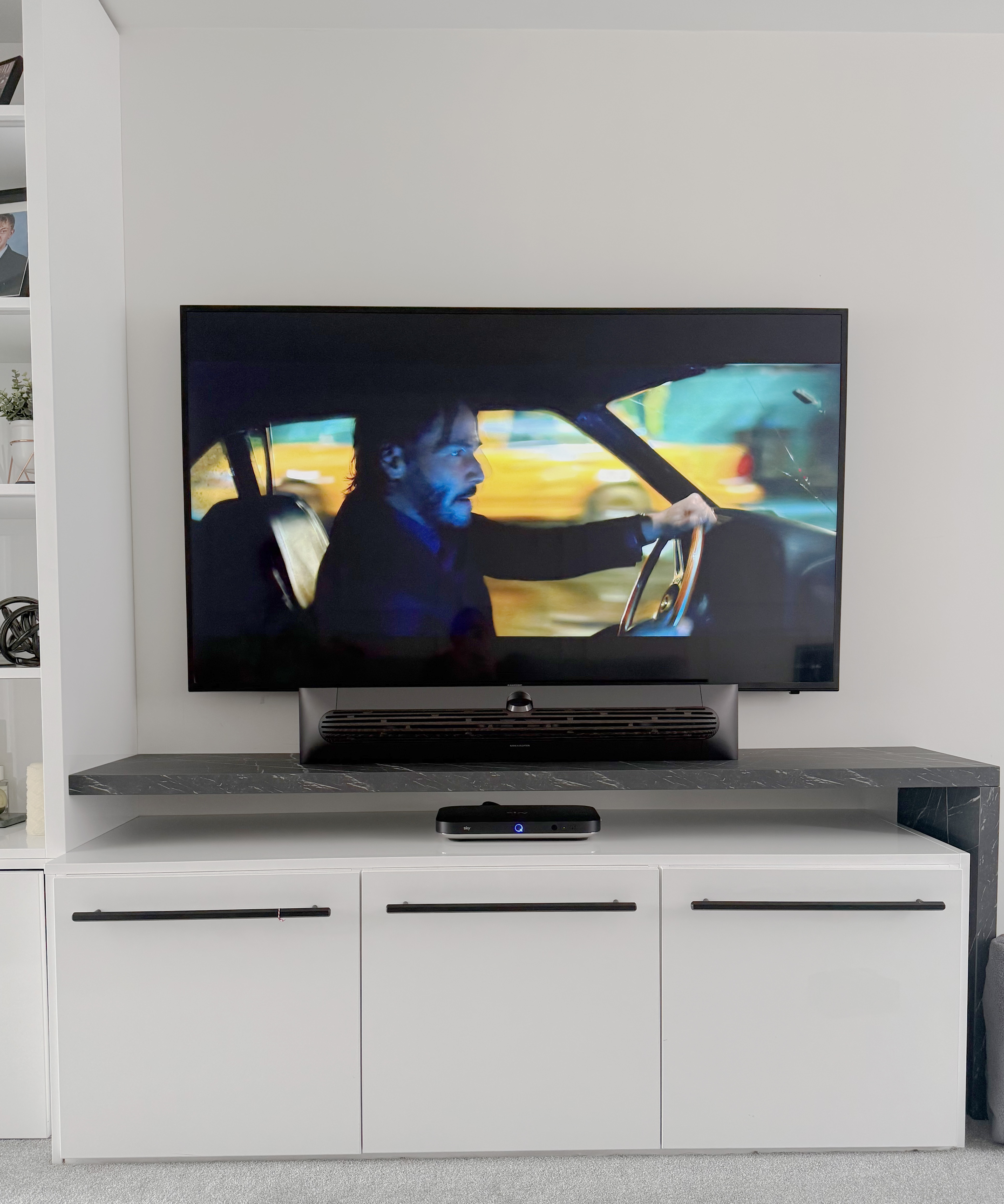 Television displaying a scene from John Wick: Chapter 2 with the soundbar positioned beneath it on a media unit