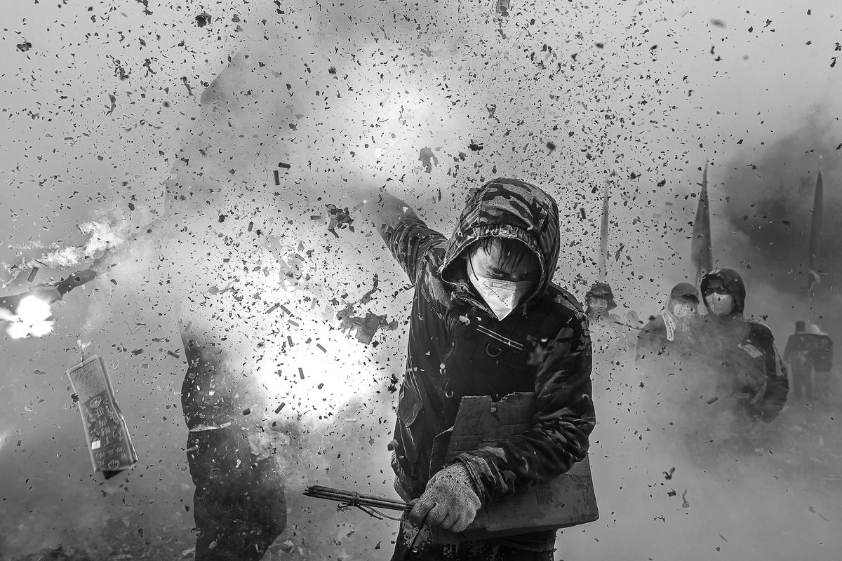 A young man wearing a mask and hood, holding firecrackers in full explosion, encapsulating the cultural tradition of &quot;frying lions&quot; to ward off evil spirits and pray for peace and prosperity.