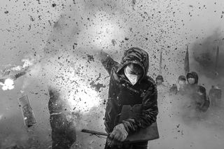 A young man wearing a mask and hood, holding firecrackers in full explosion, encapsulating the cultural tradition of &quot;frying lions&quot; to ward off evil spirits and pray for peace and prosperity.