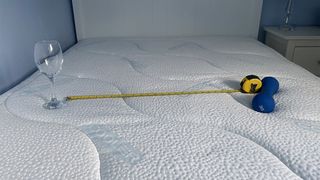 A weight, wine glass, and tape measure balanced on the Sleepeezee Cool Rest 1800 Mattress demonstrating motion isolation