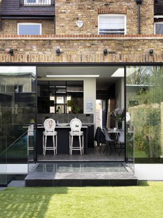 A modern house with a green lawn and large screen doors leading into a kitchen