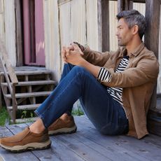 A person sat down leaning against a wooden post wearing Skechers shoes