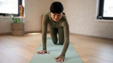 Woman setting up to do the Superman exercise on yoga mat in home studio, stretching out and wearing workout clothes