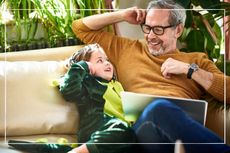 Young grandparent sitting on sofa and smiling with grandchild who is wearing a dinosaur onesie