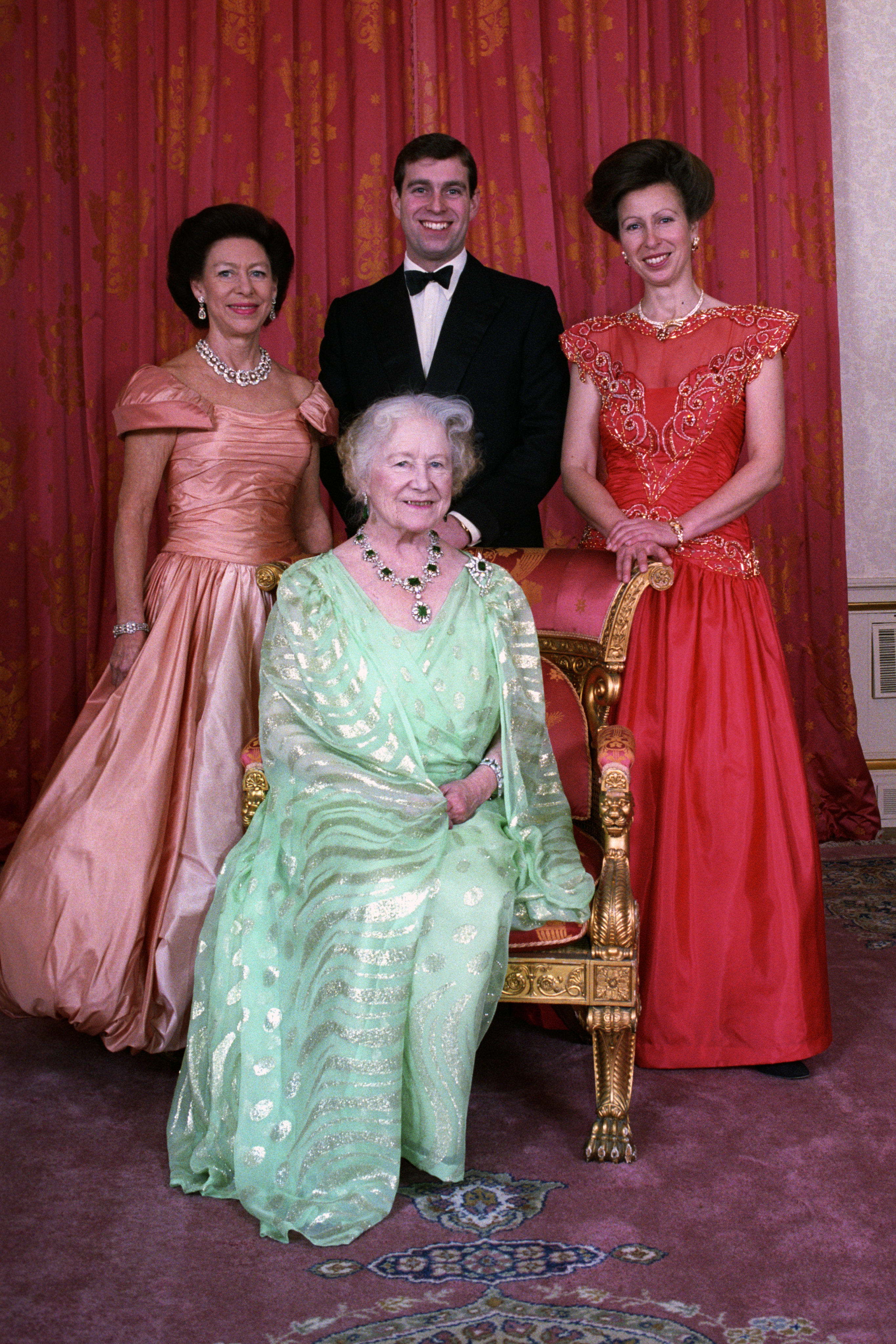 Princess Margaret, Prince Andrew, Princess Anne and the Queen Mother wearing formalwear and posing around a chair at the Dance of the Decades