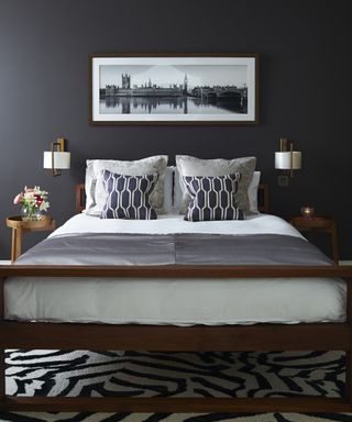 A black bedroom with a wooden bed, white linen and a black and white striped rug