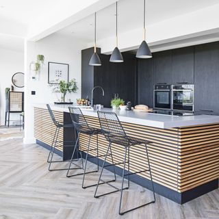 black kitchen with wooden kitchen island three wire chairs and three hanging pendants