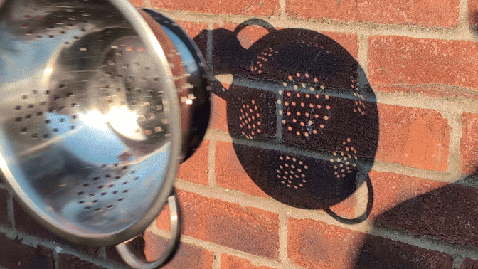 gif of a colander shadow on a wall, and as it is moved away from the wall, the colander holes in the shadow change shape to that of the solar eclipse