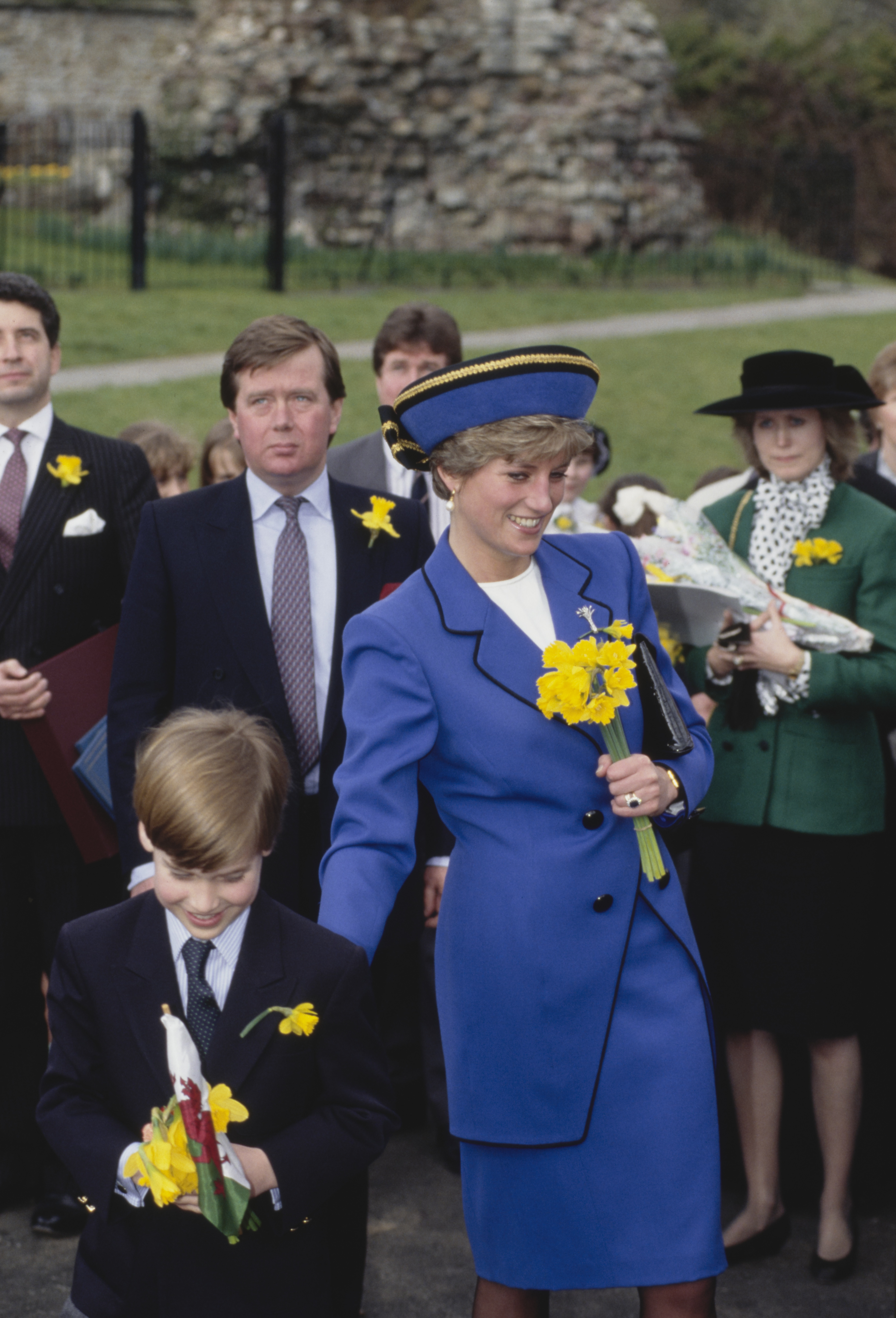 Princess Diana wearing a blue suit holding daffodils next to Prince William